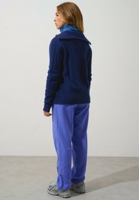 Marinblå stickad tröja med hög krage och kabelmönster, tillsammans med ljuslila byxor. Svarta och silverfärgade sneakers fulländar looken.