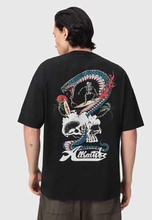 Mand iført sort t-shirt med farverigt motiv af et skelet, der surfer inde i en slange, som er snoet omkring to kranier, med teksten "Allsaints" nedenunder.