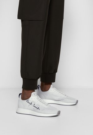 Witte Paul Smith sneakers gedragen met zwarte omgeslagen broeken, met het kenmerkende logo aan de zijkant en een textuurrijke zool.