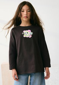Czarny, długi rękaw t-shirt z kolorową grafiką misia w stylu kreskówkowym na klatce piersiowej, połączony z jasnoniebieskimi dżinsami.