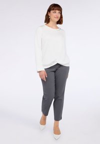 Maglietta bianca a maniche lunghe con orlo annodato, abbinata a pantaloni grigi su misura e décolleté bianche a punta. Design semplice e texture morbida.