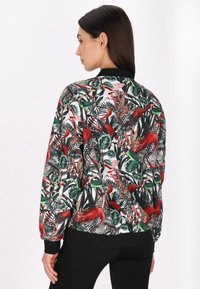 Bloemen bomberjack met een levendig patroon van rode vogels en groene bladeren. Heeft een zwarte geribbelde kraag en manchetten, gladde stoftextuur.