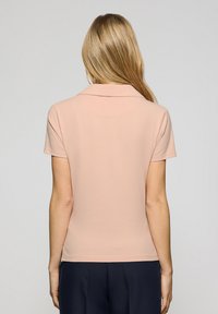 Jasnoróżowa koszulka polo z krótkimi rękawami, kołnierzykiem i gładką fakturą, prezentowana na modelu widzianym z tyłu.