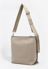 Beżowa torba na ramię o gładkiej fakturze, wyposażona w zapięcie na zamek, regulowany materiałowy pasek oraz przednią kieszeń z zatrzaskiem.