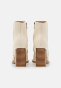 Botas de tobillo beige hechas de cuero suave, con puntera cuadrada, cierre de cremallera y un tacón de madera bloque a rayas.