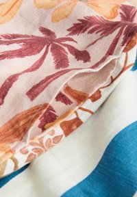 Textiles superposés, présentant un motif floral rouille et orange sur un fond clair, accompagnés de tissus unis bleu et crème.