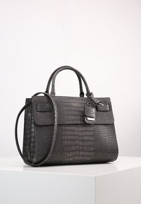 Czarna torebka Guess z materiału imitującego krokodylą skórę, z górnymi uchwytami, odpinanym paskiem na ramię oraz małym zapięciem z przodu.