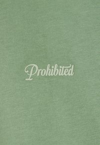 Tissu en coton vert clair avec le mot "Interdit" brodé en blanc, dans une police cursive, centré sur le matériau.
