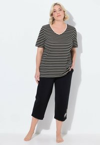Camiseta de rayas negra y beige con escote en V combinada con pantalones cortos negros que tienen un detalle de bordado floral. Casual, de tela suave.