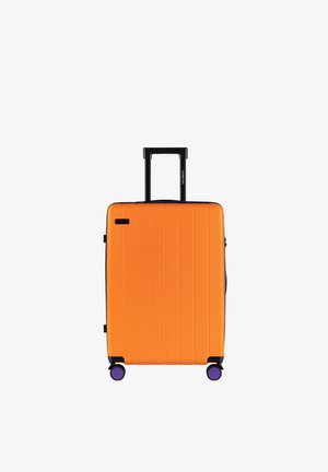 Harde koffer in fel oranje met verticale groeven, een uitschuifbare zwarte handgreep en vier paarse wielen voor mobiliteit.