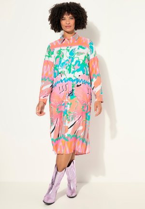 Kleurrijke button-up jurk met lange mouwen, voorzien van abstracte patronen in roze, groen en blauw. Gecombineerd met glanzende lavendelkleurige cowboylaarzen.