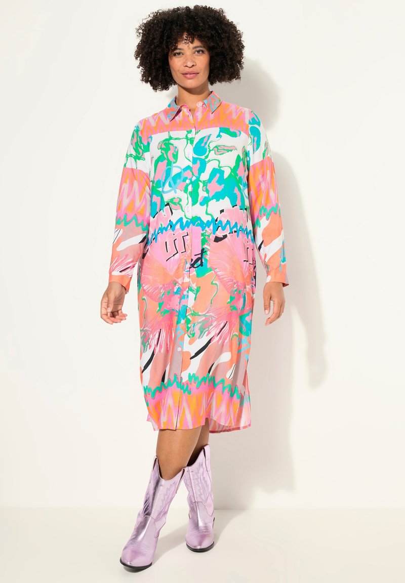 Robe boutonnée colorée à manches longues, présentant des motifs abstraits en rose, vert et bleu. Associée à des bottes de cowboy lavande brillantes.