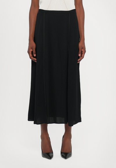 Jupe maxi noire en tissu léger avec une texture lisse, présentant des détails de couture et une silhouette évasée. Portée avec des talons noirs.