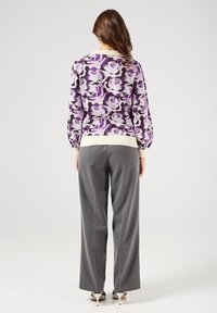 Maglione a maglia floreale viola con dettagli bianchi, abbinato a pantaloni grigi a gamba larga. Il maglione ha maniche lunghe e una vita a coste.