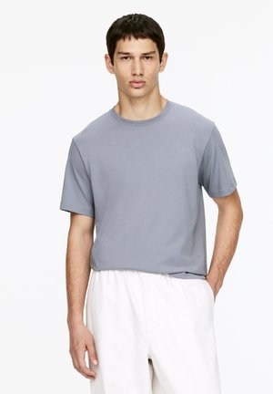 Graues Baumwoll-T-Shirt mit rundem Halsausschnitt und kurzen Ärmeln, kombiniert mit hellen, locker sitzenden Hosen. Einfaches und minimalistisches Design.
