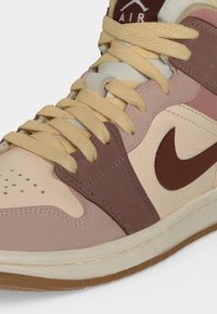 Κοντινή λήψη ενός μπεζ και καφέ παπουτσιού Nike Air με κρεμ κορδόνια, δερμάτινα και σουέντ πάνελ, και το λογότυπο Nike swoosh στο πλάι.