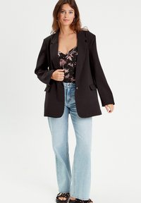 Blazer noir surdimensionné avec revers crantés, associé à un haut à imprimé floral, un jean flare bleu clair et des sandales noires avec des clous.
