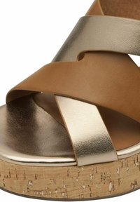 Brun och guld korsrem sandal med en metallisk finish, med en texturerad korkplattform och en slät läderöverdel.