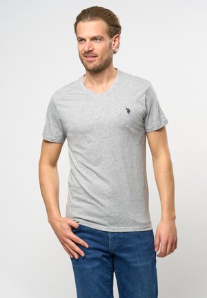 T-shirt grigia a maniche corte con scollatura a V in cotone, caratterizzata da un piccolo logo blu navy sul lato sinistro del petto e una superficie liscia. Abbinata a jeans blu.