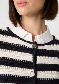 Gehaakte cardigan met afwisselend marineblauwe en crème strepen, met een ronde halslijn en zilveren drukknoopjes aan de voorkant.