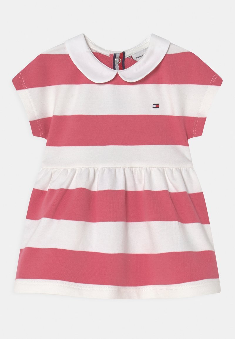 Dětské šaty s růžovými a bílými vodorovnými pruhy, krátkými rukávy, bílým límcem ve stylu Peter Pan a malým vyšitým logem vlajky na hrudi.