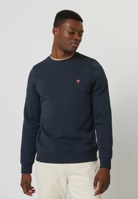 Felpa blu navy con scollo rotondo e maniche lunghe. Presenta un piccolo logo di un albero ricamato sul petto e un tessuto testurizzato.