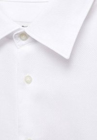 Polo blanc avec un tissu texturé, un col pointu et une patte de boutonnage avec des boutons de couleur claire.