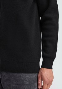 Black knit sweater with a textured finish, featuring ribbed cuffs and hem. Close-up view highlights the smooth fabric and fit.