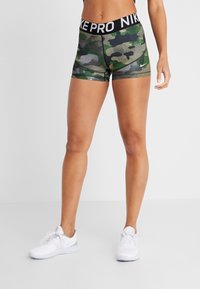 Nike Pro shorts in green camo pattern with black waistband, featuring "NIKE PRO" text and a small white logo on the lower left side.