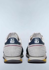 Sneaker che presentano un mix di suede bianco, blu navy e grigio, con un logo prominente sul tallone e un accento giallo sulla suola.