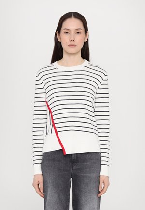Hvit genser med horisontale svarte striper og en diagonalt rød aksent. Har rund hals og ribbestrikkede mansjetter. Kombinert med mørkegrå bukser.