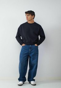 Czarna bawełniana bluza z okrągłym dekoltem, zestawiona z szerokimi niebieskimi dżinsami i białymi trampkami. Gładka tekstura i luźny krój.