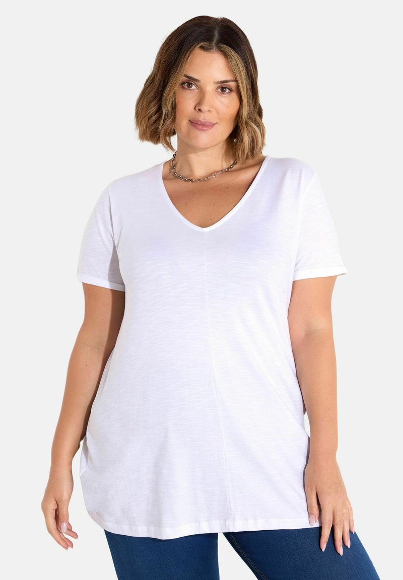 V-kaulus, lyhythihainen valkoinen paita, joka on valmistettu kevyestä kankaasta, rento istuvuus ja huomaamattomat sivusaumat, yhdistettynä sinisiin farkkuihin.