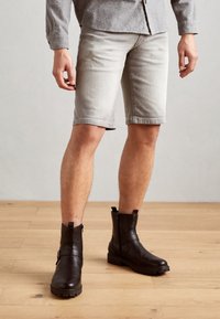 Shorts in denim grigio chiaro con un design aderente, orlo arrotolato; abbinati a stivaletti marrone scuro alla caviglia con zip laterale e dettaglio a fibbia.