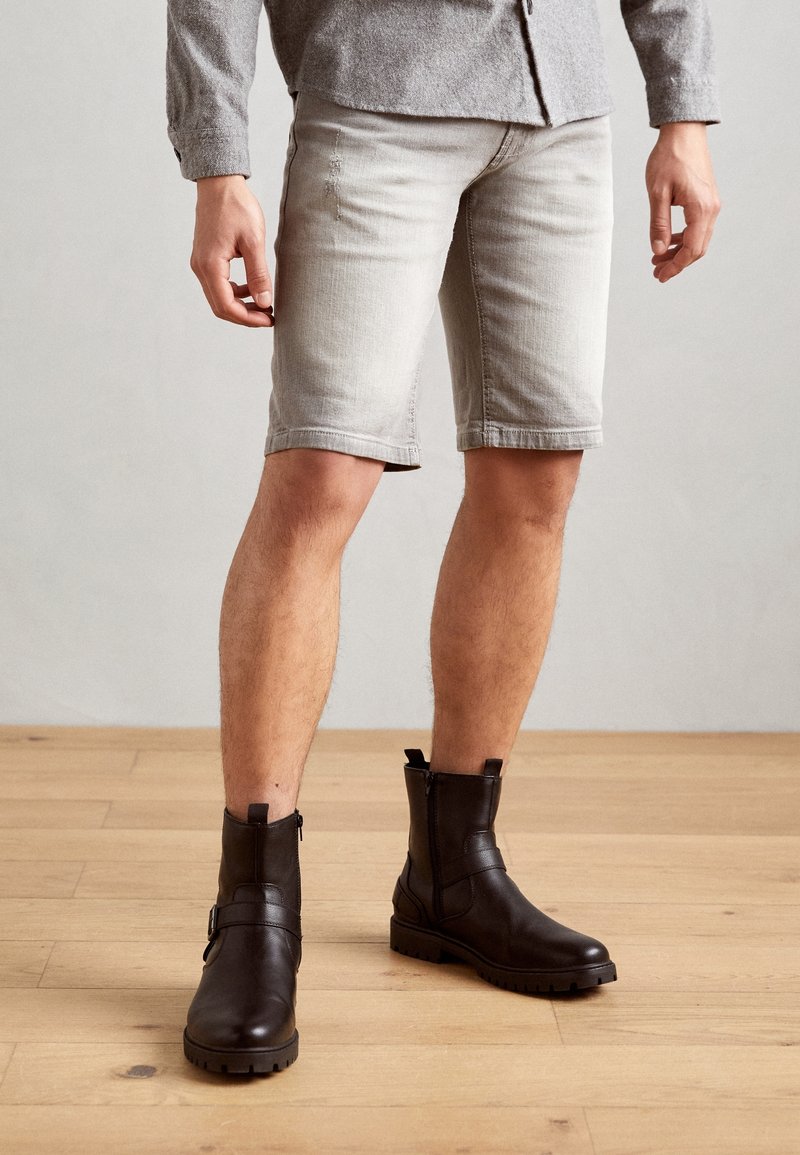 Shorts in denim grigio chiaro con un design aderente, orlo arrotolato; abbinati a stivaletti marrone scuro alla caviglia con zip laterale e dettaglio a fibbia.