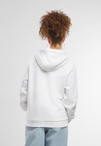 Hoodie bianco con cappuccio regolabile, vestibilità comoda e polsini a coste. Abbinato a jeans azzurri a vita alta, design minimalista.
