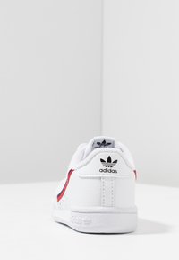 Vit sneaker med röda och blå accenter, övre del av texturerat läder, vadderad krage, logotyp på hälen och texturerad sula för ökad grepp.