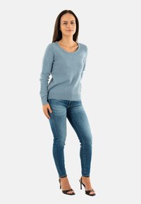 Maglione azzurro chiaro con scollo a giro, maniche lunghe e orlo a costine abbinato a jeans skinny blu scuro e sandali neri con tacco alto.