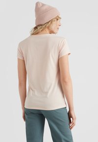 Lichtroze t-shirt met korte mouwen en een iets getailleerd ontwerp, gecombineerd met turquoise broek. Wolachtige lichtroze muts voegt een contrasterende textuur toe.