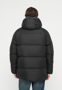 Fekete puffdzseki kapucnival, steppelt mintával, vastag töltettel és logó részlettel a galléron. Könnyű anyag.