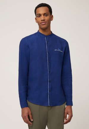 Donkerblauwe lange mouwen shirt van linnen met een collarioos ontwerp, knoopsluiting aan de voorkant en een klein wit accentvakje.