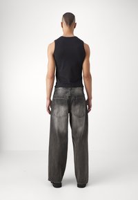 Svart ärmlös skjorta kombinerad med löst sittande, blekgrå jeans. Jeansen har bakfickor och subtila sömnadsdetaljer.