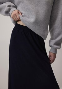 Felpa grigia con spalle scese, abbinata a una gonna nera scura con vita elastica. Focus sulla texture del tessuto e sulla vestibilità. Nessun motivo visibile.