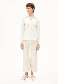 Witte button-up shirt, lange mouwen, lichtbeige wijde broek en bleekroze schoenen. Vlotte stof, eenvoudige kraag en knoopdetails.