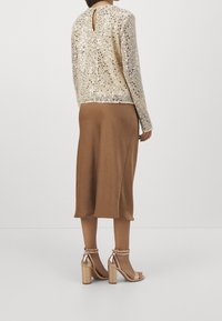 Zlatý top s dlouhým rukávem zdobený flitry a s vykrojením na zádech, kombinovaný s hnědou midi sukní a metalickými sandály na blokovém podpatku.