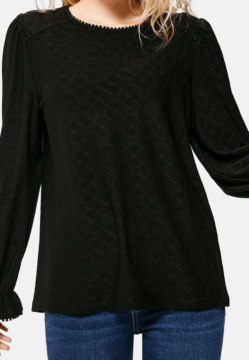 Top negro tipo pulóver con patrón texturizado, mangas largas abullonadas y detalle de escote en forma de ondas. Combinado con jeans de mezclilla azul.