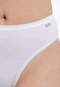 White cotton panties feature a smooth texture, elastic waistband, and a small branded tag on the side. Simple, classic design.