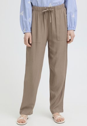 Pantaloni largi maro deschis, cu buzunare aplicate în față și talie cu șnur, purtați cu o bluză albastră și sandale albe cu barete.