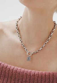 Collar de cadena de plata con eslabones entrelazados, que presenta un cierre redondo y un charm rectangular. La textura es pulida y suave.