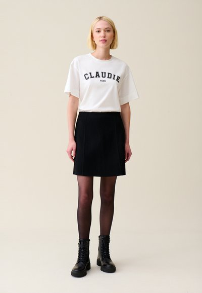 Camiseta blanca de algodón con "CLAUDIE PARIS" en letras negras, combinada con una falda negra acampanada y botas de tacón negro con cordones.